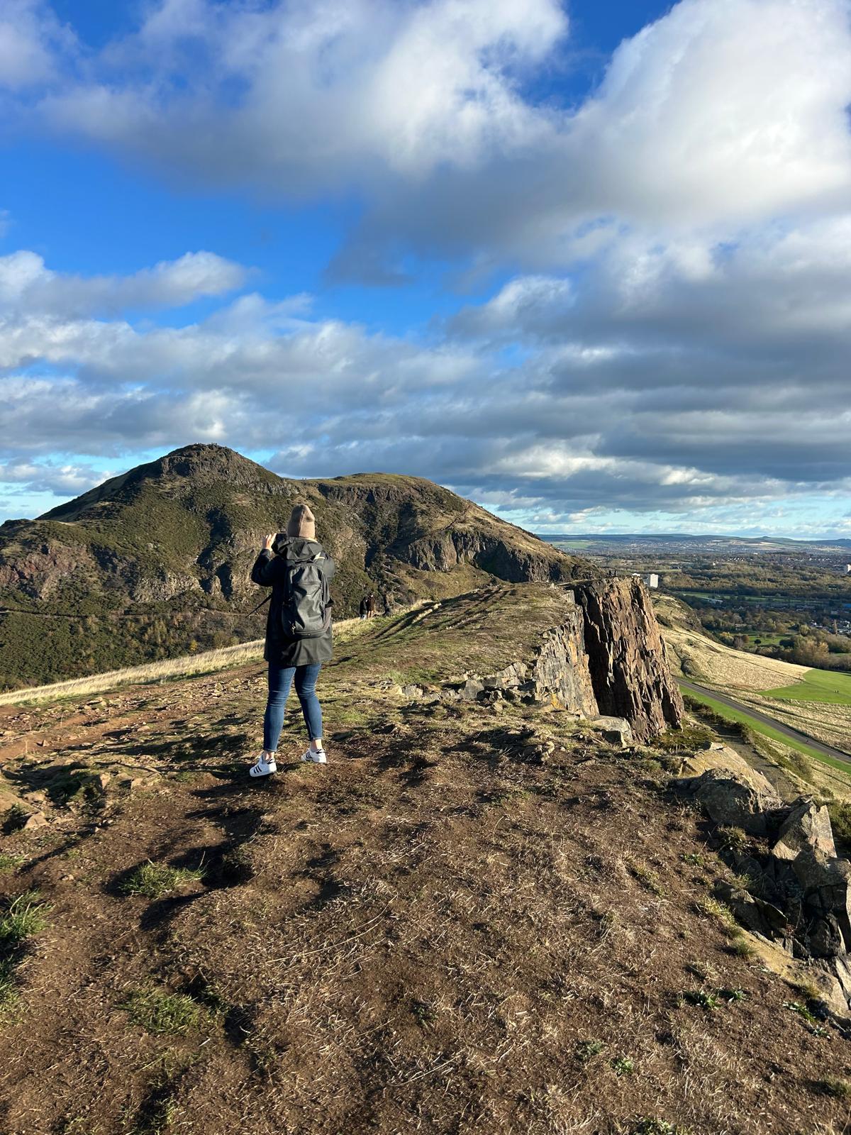 personne prenant en photo un panorama montagneux au sommet de la colline Arthur's Seat à Édimbourg