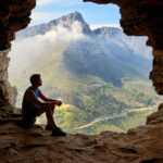 voyageur contemplant une vallée montagneuse depuis l'entrée d'une grotte