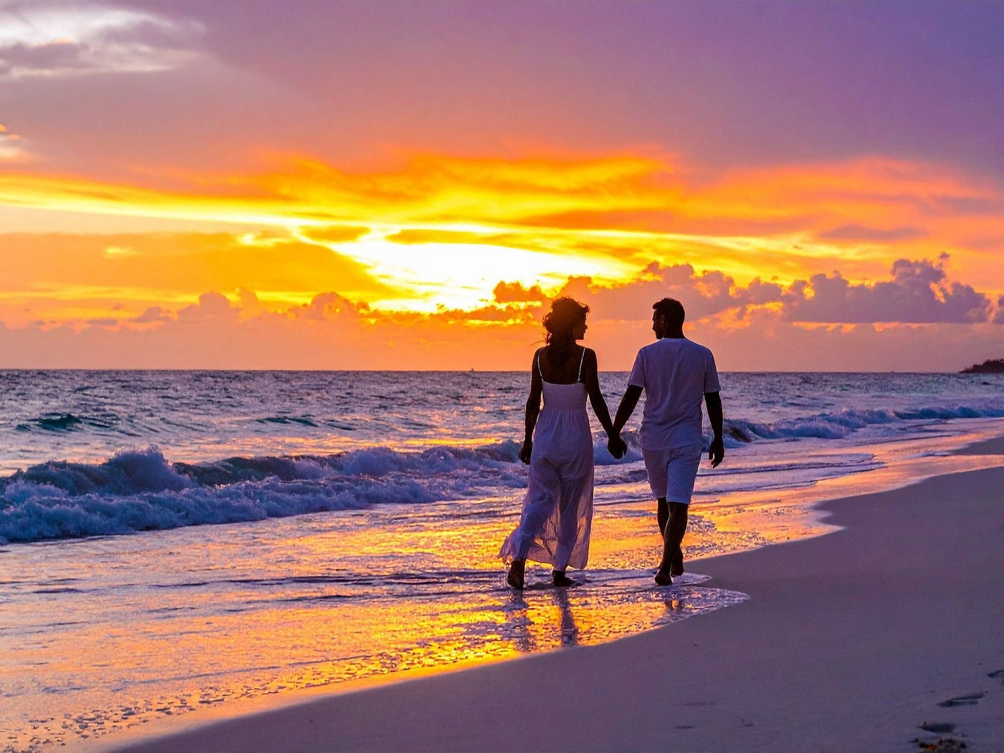 couple marchant main dans la main sur la plage au coucher du soleil